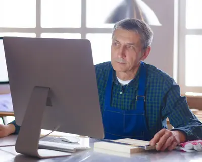 Mann in blauer Latzhose sitzt vor einem Computer